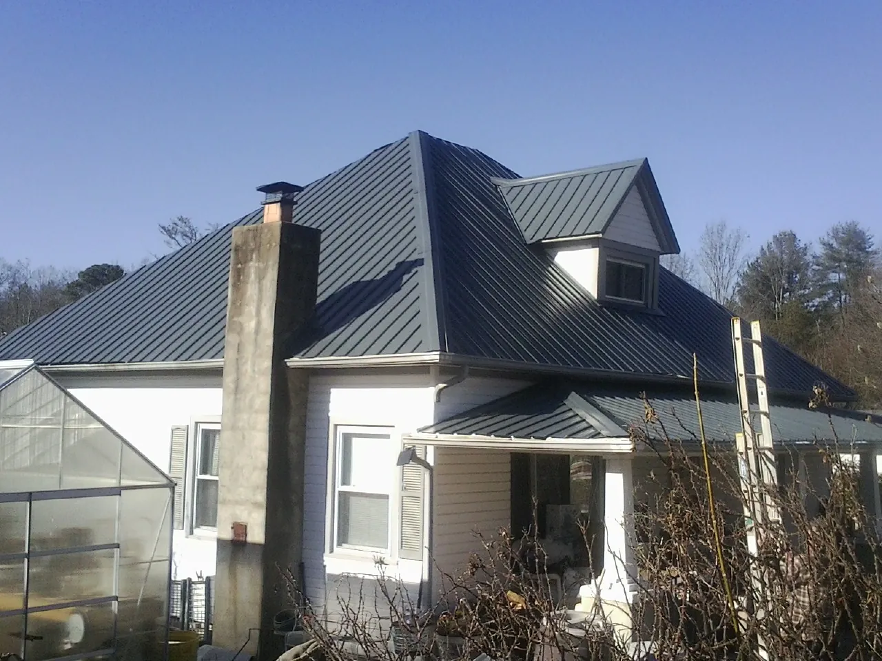 Dark blue standing seam metal roof on a white farmhouse with dormer — Slate & Tile Roof Repair by Roofing Brothers in Colman