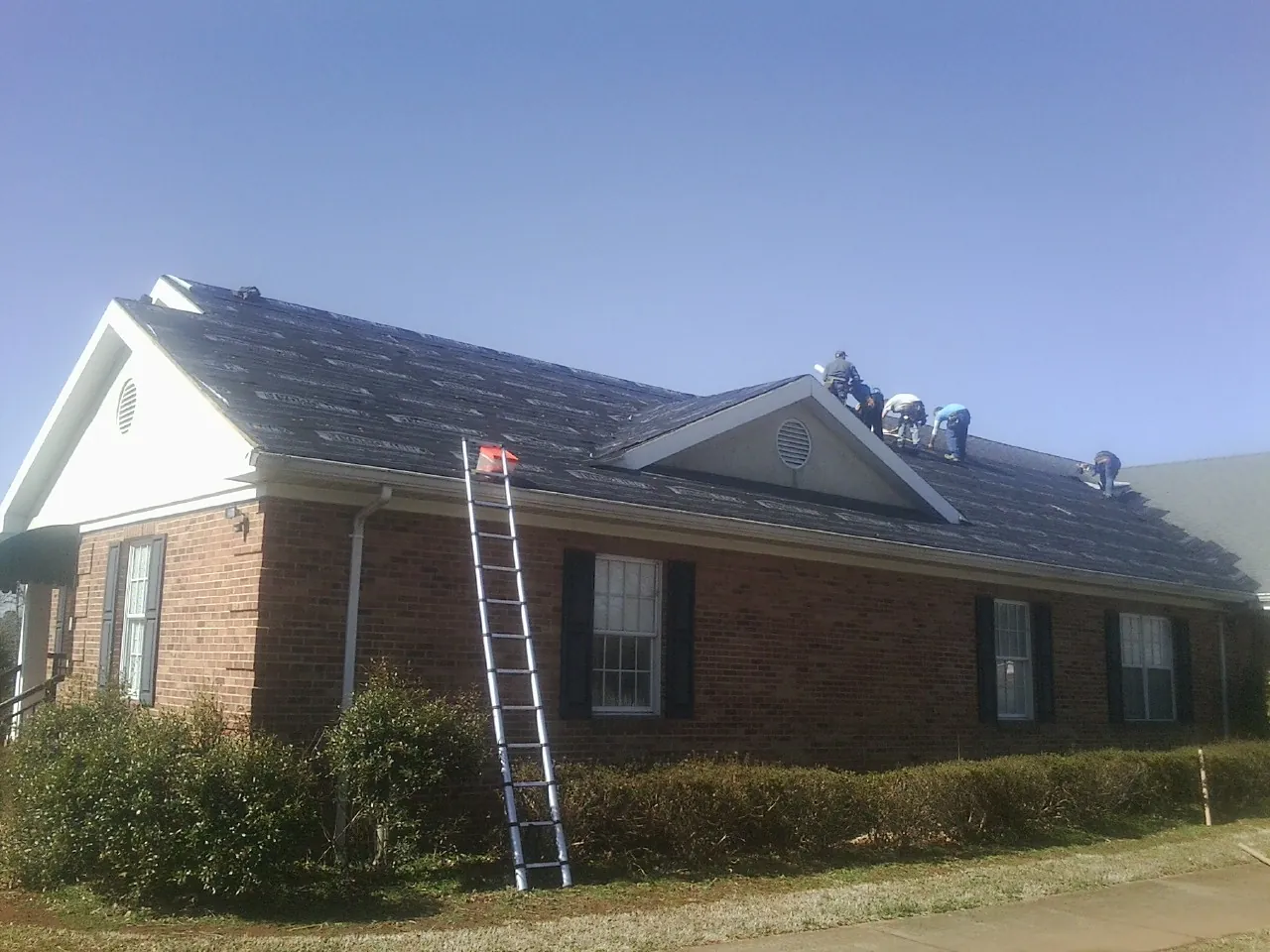Crew tearing shingles off a brick ranch roof with a ladder set — Metal Roof Repair work by our crew in Colman