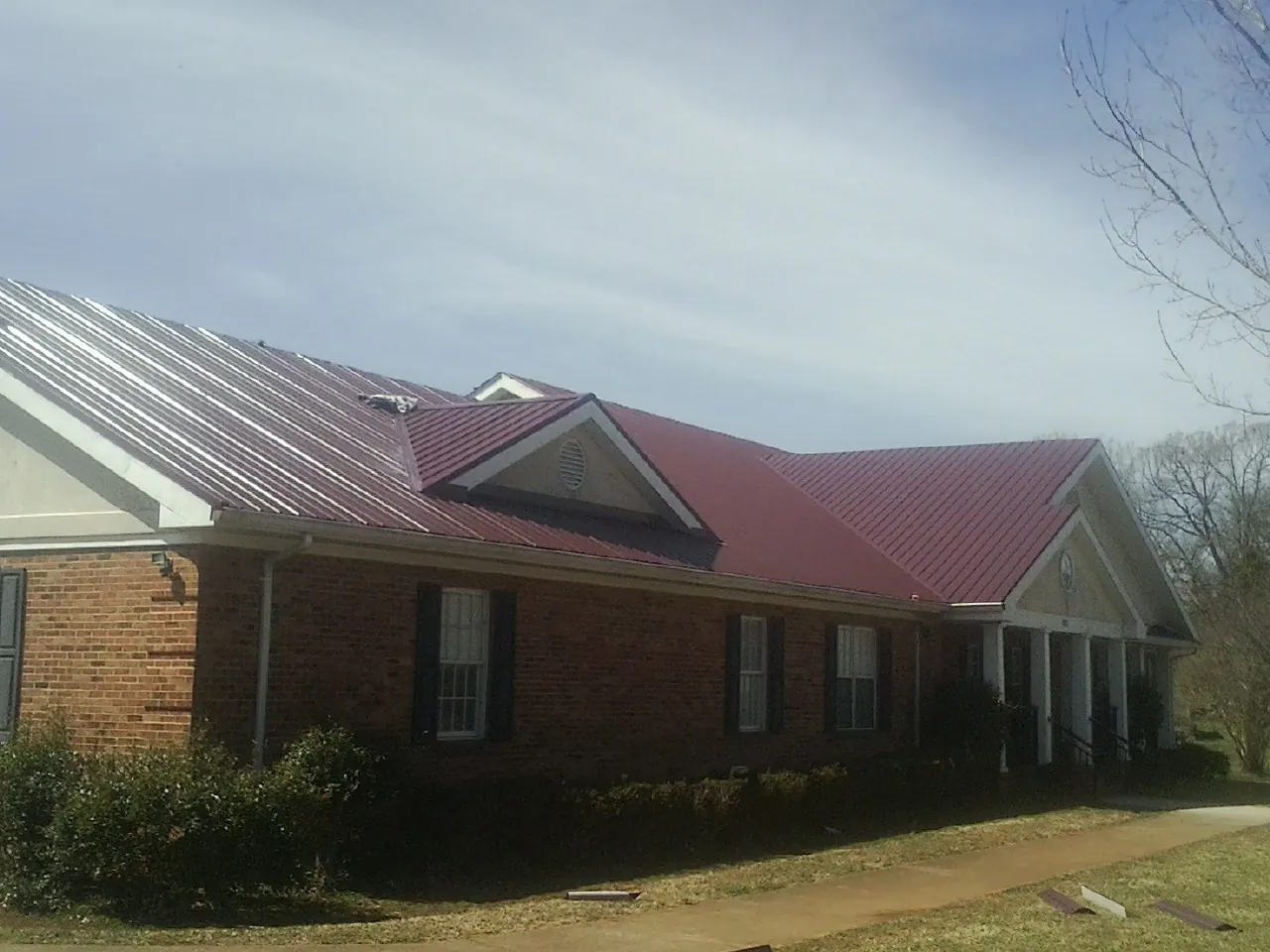 Red metal roof with gabled entries on a long brick building, from a Hail Damage Roof Repair job in Colman