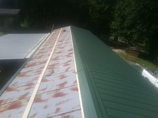 Old rusted panels beside newly installed green metal roofing — Wind Damage Roof Repair by Roofing Brothers in Colman